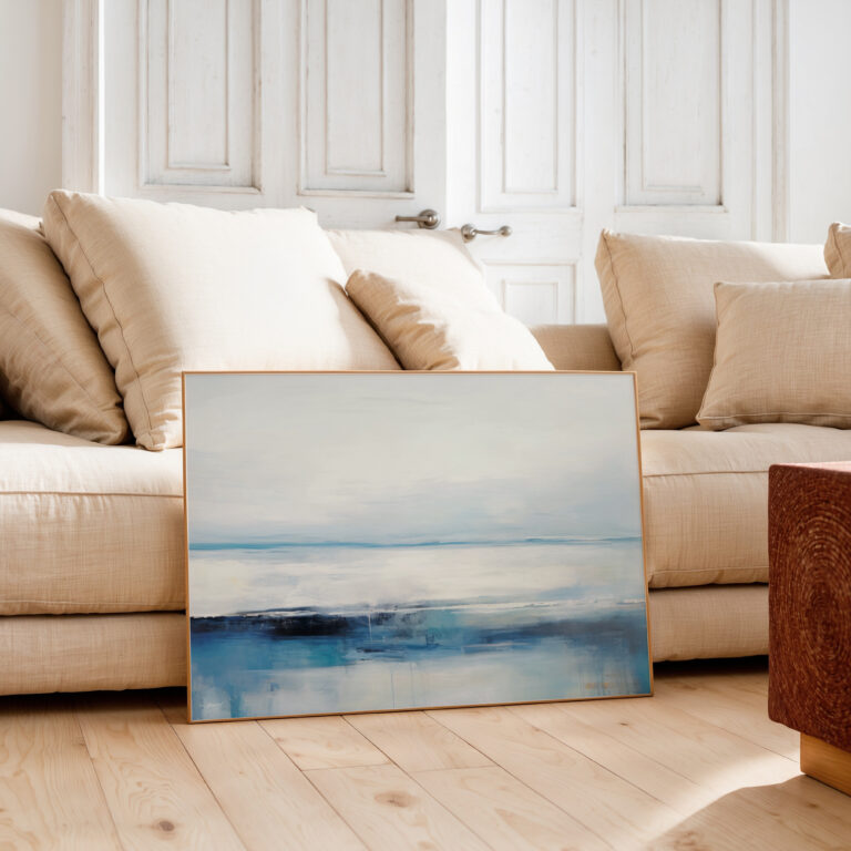 Abstract blue and white coastal artwork leaning against beige sofa in minimalist living room.