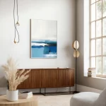 Abstract blue ocean artwork above mid-century wooden cabinet in modern coastal living room