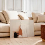 Modern abstract art canvas with terracotta tones against neutral beige sofa in minimalist room.