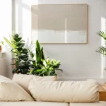 Minimalist beige abstract art framed above white sofa with lush green plants nearby.