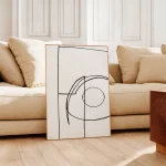 Minimalist black line art in wooden frame against neutral beige sofa
