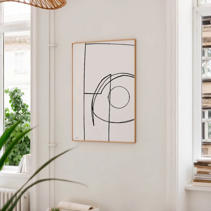 Minimalist black line art in wooden frame with indoor plant against white wall.