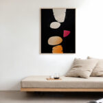 Abstract geometric art with orange shapes on black background above minimalist wooden bed.