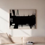 Bold black brushstroke abstract art hung above cream sofa in minimalist white room.