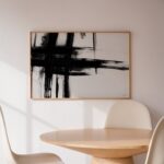 Abstract black brushstroke artwork in minimalist white interior with wooden table