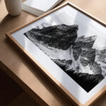Dramatic black and white mountain peaks photograph in wooden frame on rustic surface.