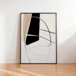 Minimalist black and beige abstract print in wooden frame leaning against white wall