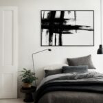 Bold black and white abstract artwork above bed in minimalist gray bedroom.