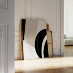 Minimalist black curve artwork leaning against white wall in bright interior with wooden flooring.