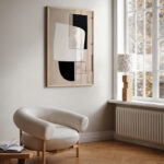 Minimalist living room corner with abstract geometric artwork and curved beige accent chair.