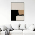 Abstract black and beige geometric artwork hangs above white sofa in modern living space.