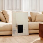 Abstract black and gray geometric artwork displayed against beige sofa in minimalist living room.
