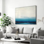 Minimalist blue ocean abstract painting above gray sofa in modern living room.