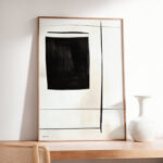 Minimalist black geometric artwork in wooden frame with white ceramic vase on display