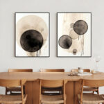 Modern abstract diptych with black and beige circles above wooden dining table.