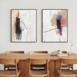 Abstract line art diptych with black frames above wooden dining table and chairs.