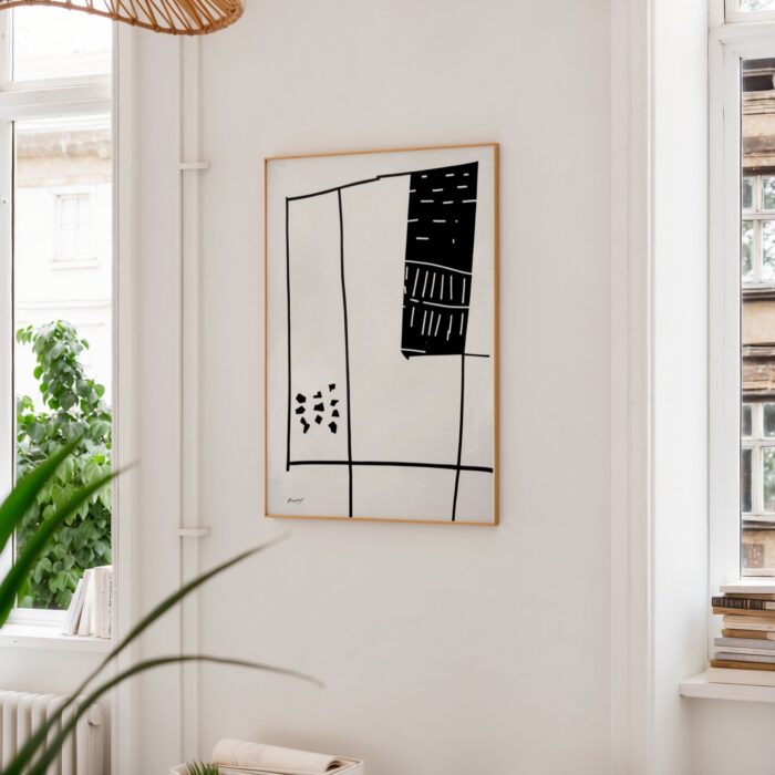 Geometric black and white abstract art framed above indoor plant in minimal interior setting.
