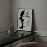 Minimalist black line drawing portrait above dark marble console with sculptural decorative accents.
