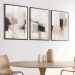 Abstract art triptych with black and beige brushstrokes above wooden dining table.