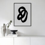 Minimalist black fluid abstract art in sleek frame above white cabinet with ceramics