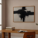 Abstract black brushstroke painting above wooden desk in light-filled minimalist space.