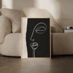 Minimalist line art facial profile in wooden frame against cream sofa