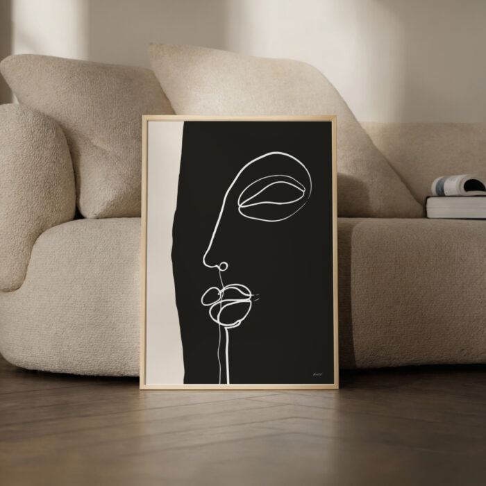Minimalist line art facial profile in wooden frame against cream sofa