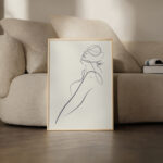 Minimalist line drawing portrait in wooden frame against soft beige sofa background