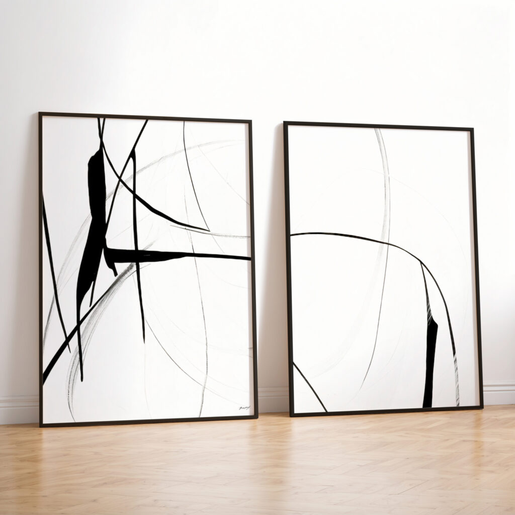 Minimalist black and white abstract line art diptych leaning against white wall on wood floor.