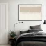 Minimalist abstract beige artwork above gray bed in contemporary bedroom with white walls.