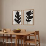 Wooden dining table with chairs beneath framed black botanical prints on beige wall.