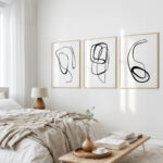 Minimalist line art triptych over bed in serene neutral bedroom with natural light.