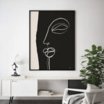 Minimalist face line drawing on black canvas above modern white console with plant.