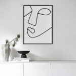 Minimalist black line art face profile on white wall above modern cabinet display.