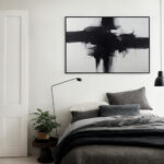 Minimalist bedroom with bold black abstract art above layered gray bedding.