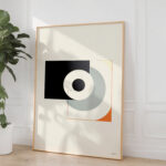 Minimalist geometric art print with black square, white circle and orange accent against white wall