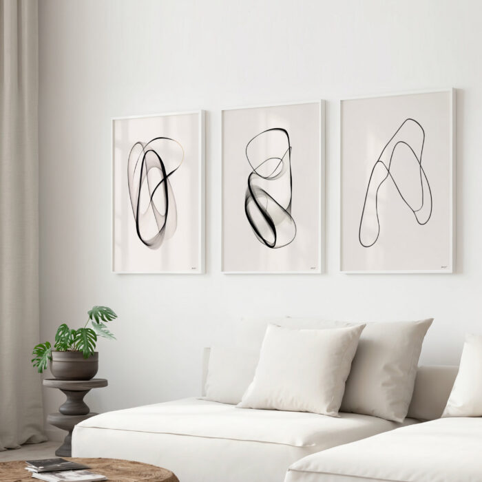 Modern black line art trio displayed above cream sofa in minimalist living space.