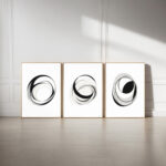 Minimalist black circular brushstrokes triptych on white canvas with wooden frames against white wall.