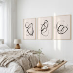 Elegant line art triptych above bed in peaceful minimalist bedroom with neutral tones.