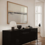 Minimalist black sideboard beneath abstract horizon artwork in bright contemporary interior space.