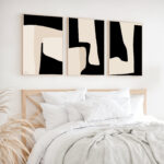 Abstract black and white triptych artwork above bed with white linens and natural accents.