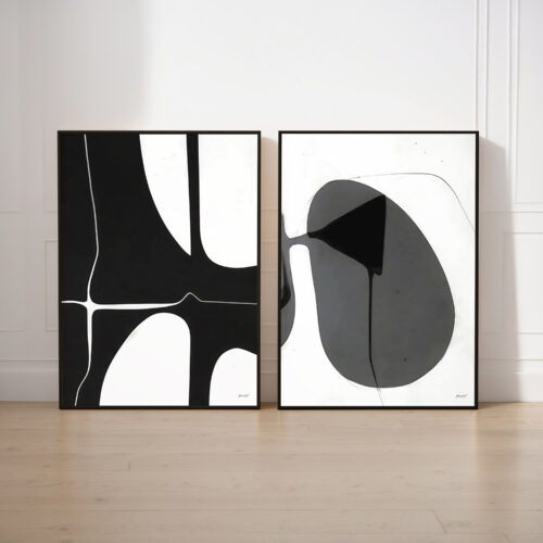 Two framed abstract artworks featuring black, white and gray geometric patterns on white wall.
