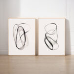 Two framed abstract artworks with fluid black brushstrokes on white backgrounds.