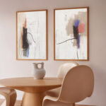 Elegant abstract line art pair above round wooden table in minimal dining corner.