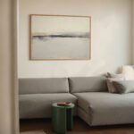 Abstract landscape artwork in muted tones above modern gray sectional sofa.
