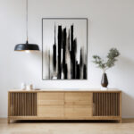 Minimalist black abstract art hanging above light oak credenza with modern pendant light.