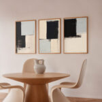 Three framed abstract artworks above a round wooden table with modern cream chairs.
