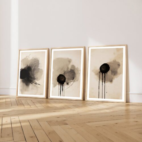 Three minimalist abstract ink paintings with circular forms leaning against white wall.