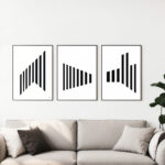 Black and white geometric triptych art displayed above modern gray sofa with plant accent.