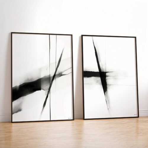 Two minimalist black and white abstract prints leaning against white wall on wooden floor.